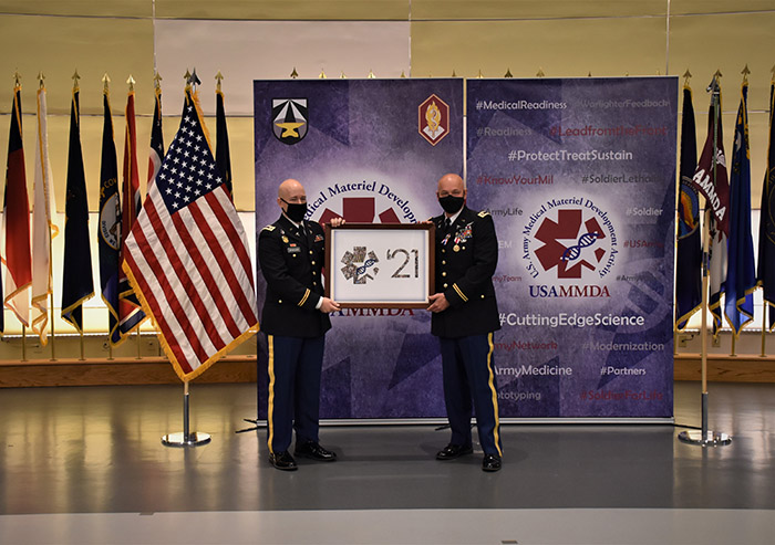 Army Maj. Scott Wynocker presents a framed 2021 USAMMDA group photo