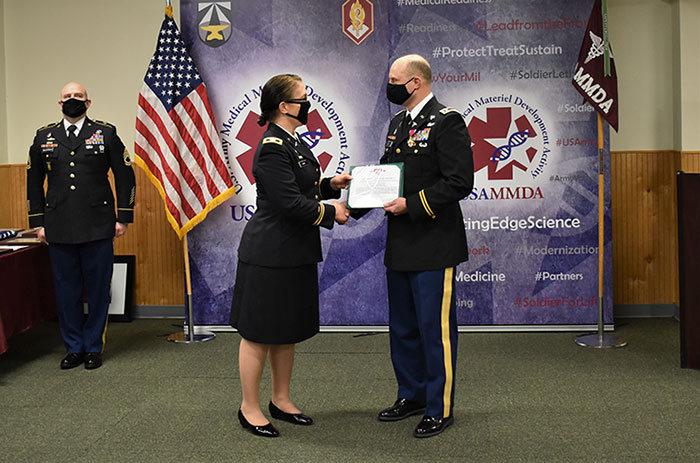 Army Col. Gina E. Adam, presents Lt. Col. Christian Cook with one of many awards and certificates